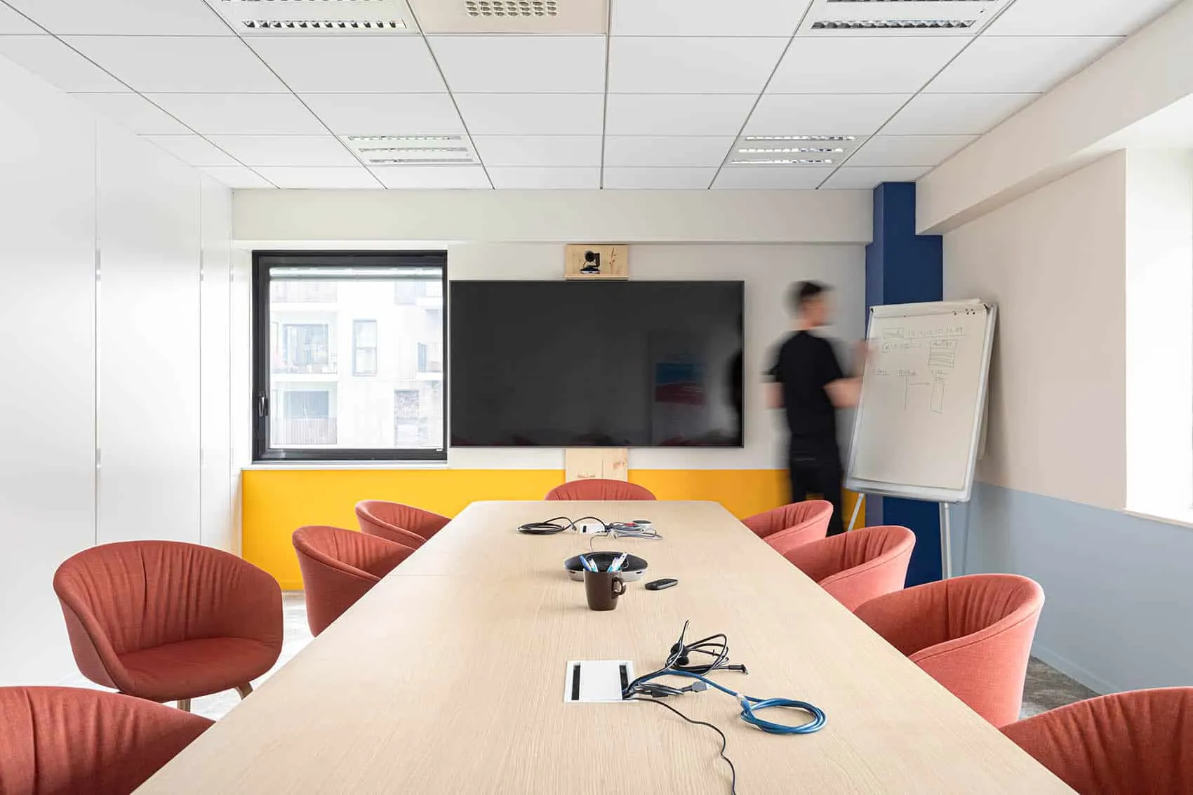 Salle de réunion des bureaux d’un éditeur de logiciel à Lyon 3e : grande table en bois et fauteuils corail