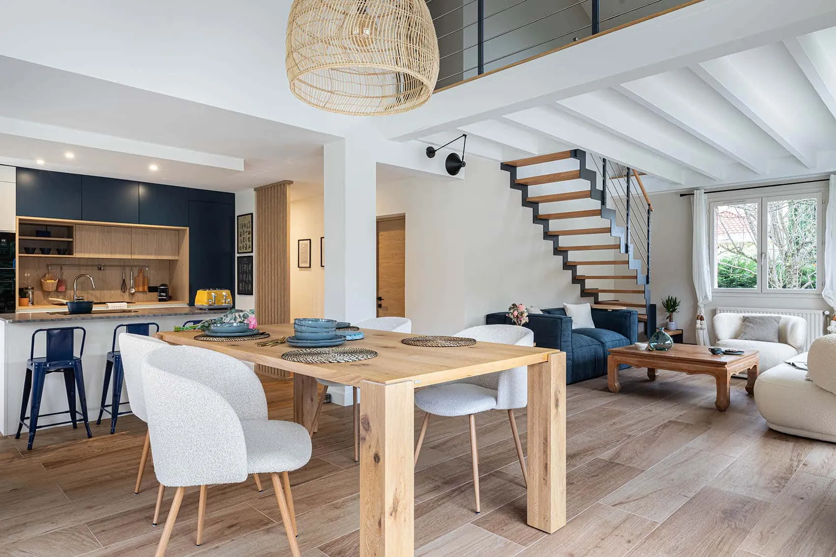 Pièce de vie de la Maison Noyer, maison des années 80 rénovée : cuisine bleue sur mesure, table en bois et escalier ouvert