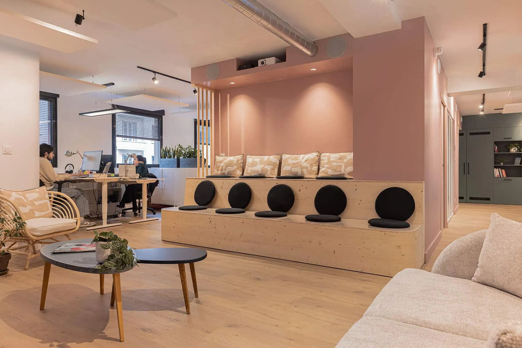 Espace de coworking des bureaux de Cap’Com à Lyon : gradins en bois sur mesure et murs rose poudré, aménagement de bureaux